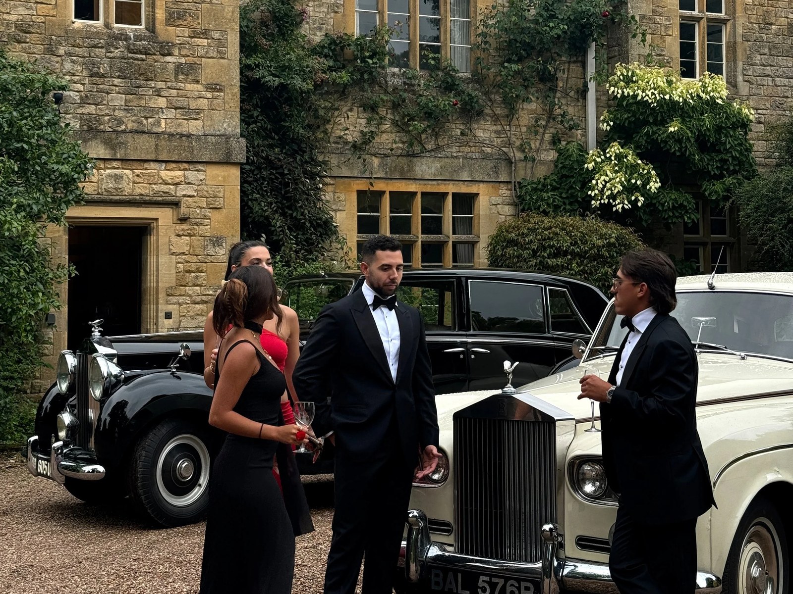 A black-tie group beside vintage Rolls-Royces at a manor